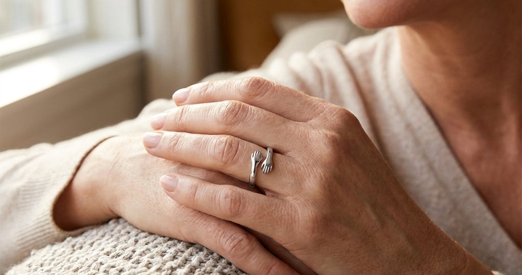 Woman's hands resting on a knit blanket, wearing the silver Hug from Heaven Ring with two small hands