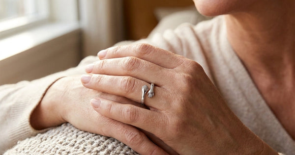 Woman's hands resting on a knit blanket, wearing the silver Hug from Heaven Ring with two small hands