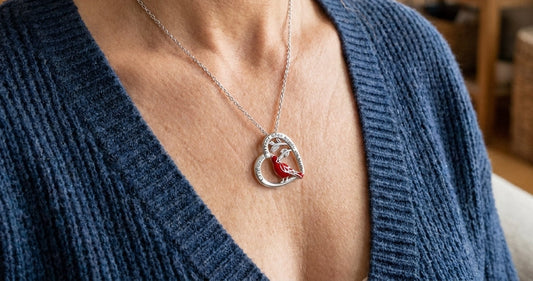 Woman in a blue knit cardigan wearing a silver heart necklace with a red cardinal on a branch