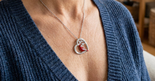 Woman in a blue knit cardigan wearing a silver heart necklace with a red cardinal on a branch