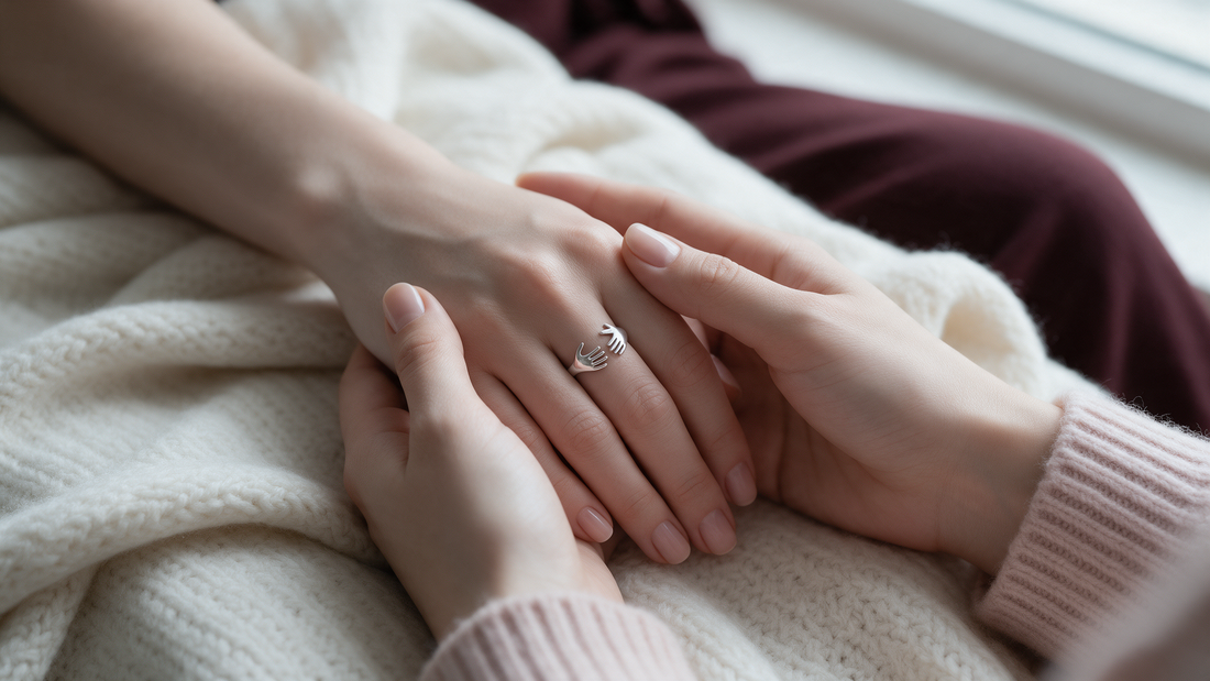 Hands holding with a silver hug ring on a cream blanket