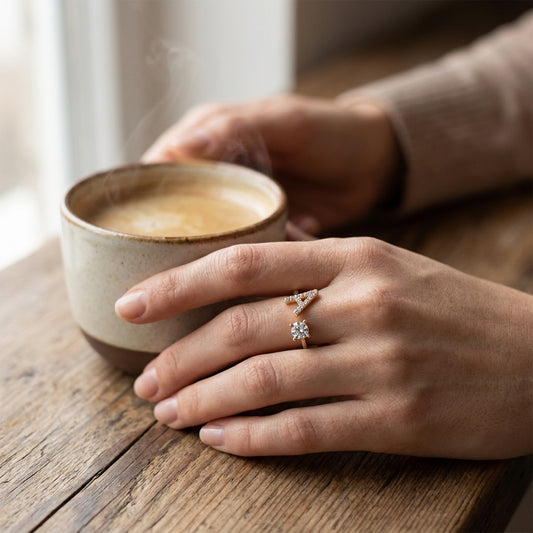 Adjustable gold initial ring with a sparkling letter A worn beside a coffee cup