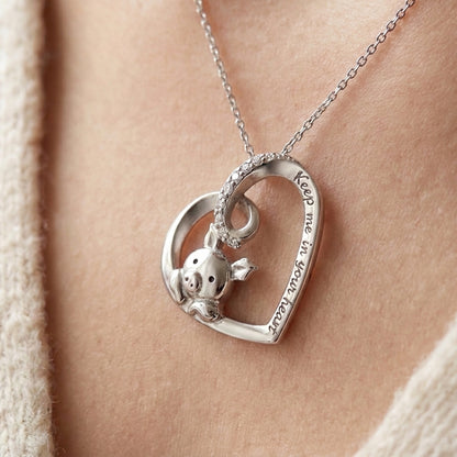 Silver heart pendant with a small pig inside the heart, a row of tiny stones on the top loop and the words Keep me in your heart engraved on the edge, shown on a fine chain (styled lifestyle photo, pendant only, chain sold separately)