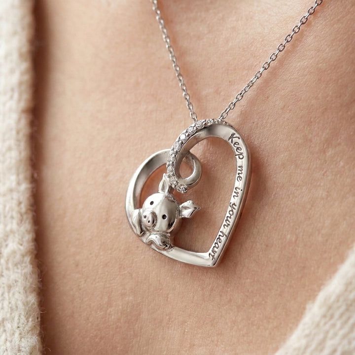 Silver heart pendant with a small pig inside the heart, a row of tiny stones on the top loop and the words Keep me in your heart engraved on the edge, shown on a fine chain (styled lifestyle photo, pendant only, chain sold separately)