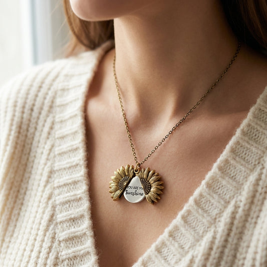 Antique gold-tone sunflower locket necklace worn open, showing the engraved inner disc that reads You are my Sunshine (styled lifestyle photo)